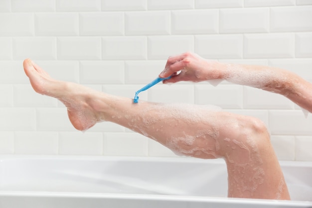 Eine Frau im Badezimmer rasiert sich mit einem Rasiermesser die Beine. Nahaufnahme einer Hand mit einem Rasiermesser.