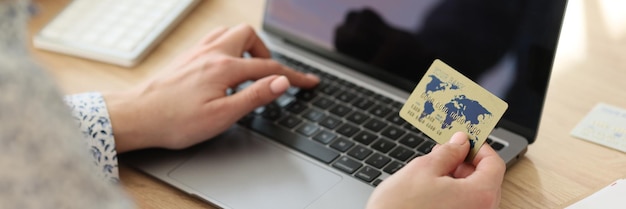 Eine Frau im Büro wählt eine Kreditkartennummer auf der Laptop-Tastatur