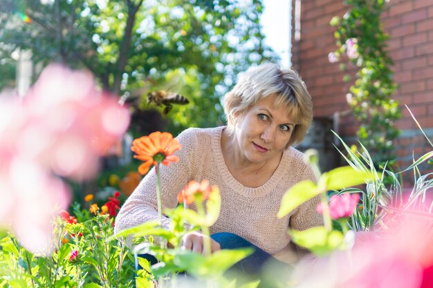 Eine Frau im Garten wählt Blumen für Setzlinge aus. Eine Frau mittleren Alters sieht überrascht aus. Sie arbeitet im Dorf.