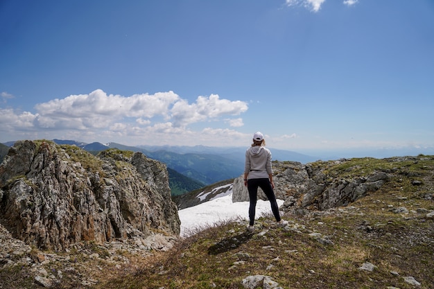 Eine Frau im grauen Kapuzenpulli, der auf Felsen vor Himmelhintergrund steht