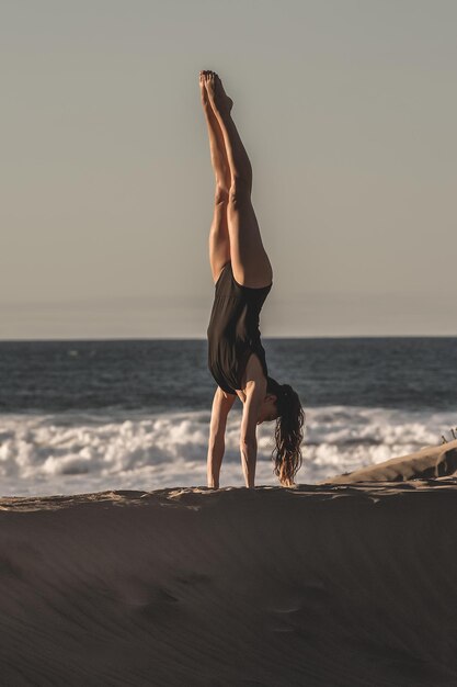 Eine Frau im Handstand am Strand in voller Länge
