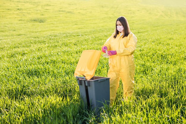 Eine Frau im Schutzanzug steht mitten auf einem Feld und hält eine Plastikflasche in den Händen