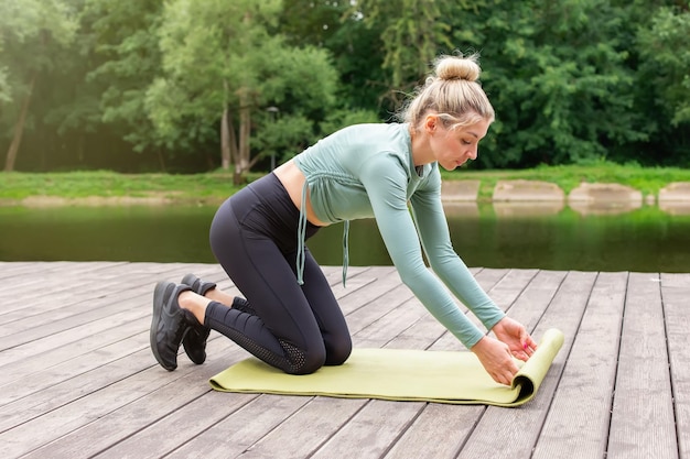 Eine Frau im Sommer am Teich entspannt sich auf einer grünen Turnmatte und bereitet sich auf den Sport vor