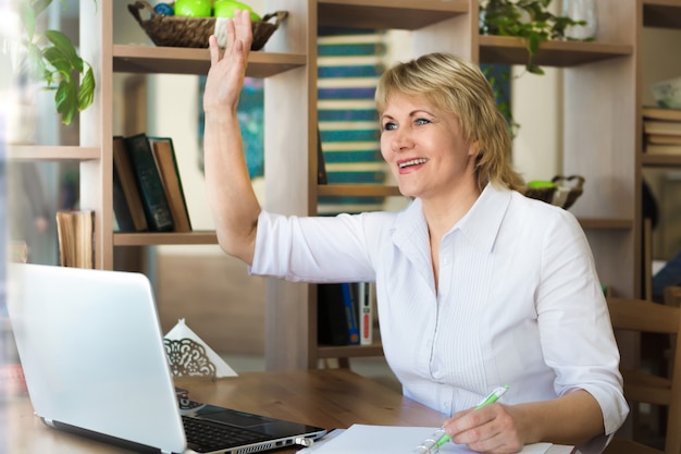 Eine Frau im weißen Hemd arbeitet im Büro an einem Laptop. Eine Frau mittleren Alters begrüßt Sie mit der Hand in einem Café.