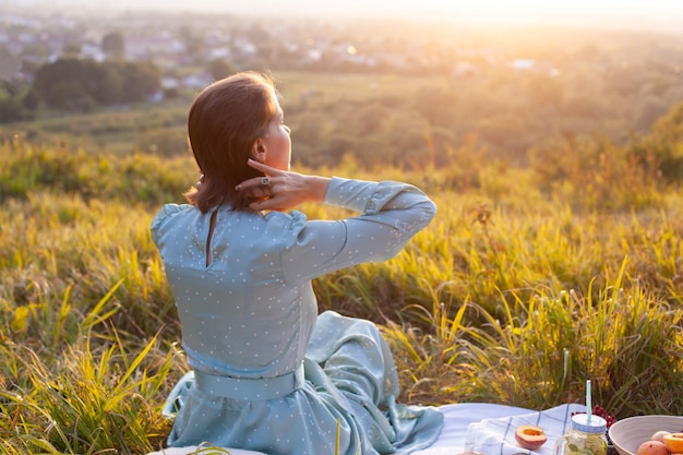 Eine Frau in blauem Kleid sitzt auf einem Picknick in einem Park mit Panoramablick