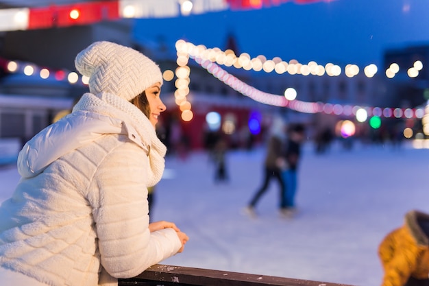 Eine Frau in der Nähe der Eisbahn Schlittschuhlaufen Silvester und Weihnachtslichterkette Eis- und Schneestimmungskonzept