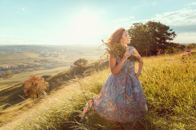 Eine Frau in einem blauen Kleid steht mit einem Blumenstrauß in der Hand auf einem Feld.