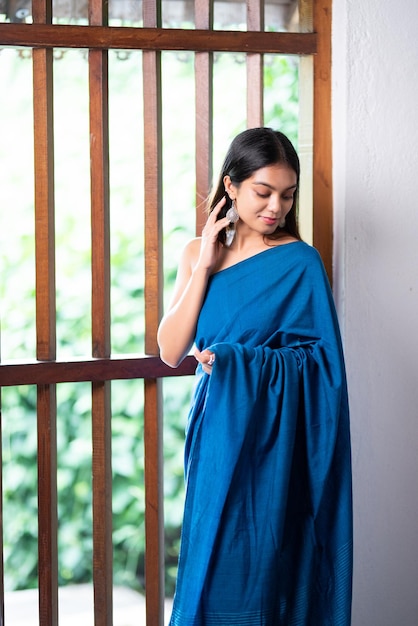Foto eine frau in einem blauen saree steht vor einem fenster.