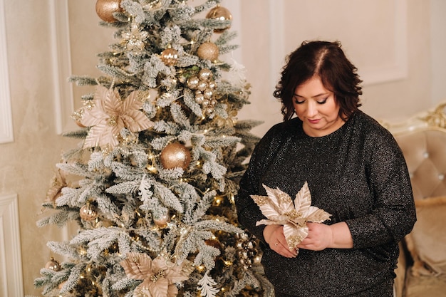 Eine Frau in einem dunklen Kleid, die neben einem Weihnachtsbaum in einem Interieur steht, das entworfen wurde, um Weihnachten und Neujahr zu feiern