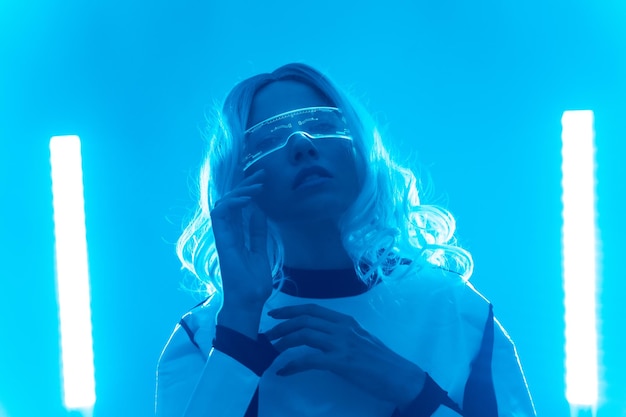Eine Frau in einem futuristischen Anzug und Brille mit blauem Licht oder Metaverse-Konzept denken und schauen