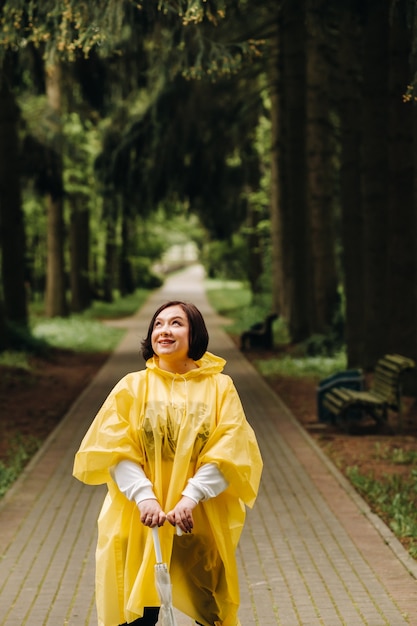 Eine Frau in einem gelben Regenmantel und einem Regenschirm spaziert im Sommer im Park und Garten