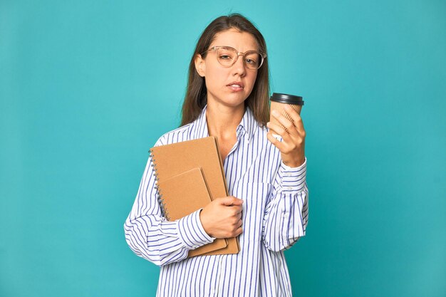 Eine Frau in einem gestreiften Hemd hält eine Kaffeetasse in der Hand und schaut auf ihr Telefon.