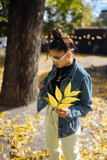 Eine Frau in einem Herbstpark hält ein gelbes Blatt