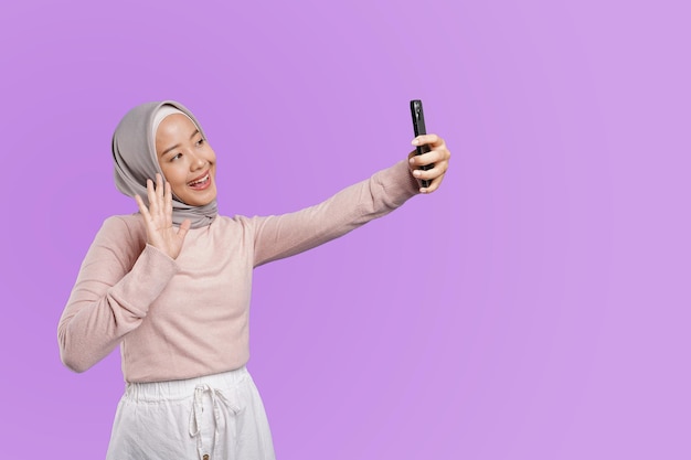 Eine Frau in einem Hijab macht mit ihrem Telefon ein Selbstporträt und führt einen Videoanruf mit ihrer Familie durch