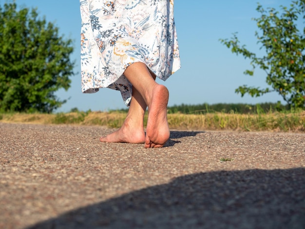 Eine Frau in einem Kleid geht barfuß über den Asphalt. Rückansicht. Das Konzept von Reisen, Erholung, Urlaub, Freiheit