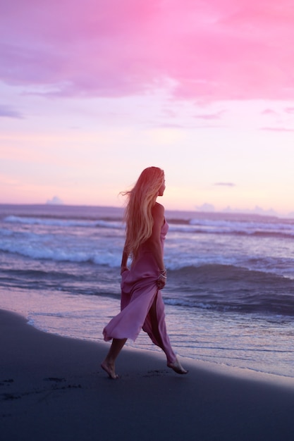 Eine Frau in einem Kleid geht bei Sonnenuntergang ans Meer