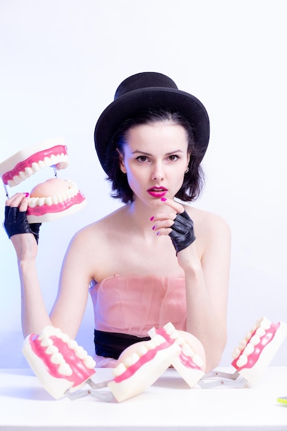 Eine Frau in einem Kleid und Hut sitzt an einem Tisch und hält ein Modell ihrer Zähne hochqualitatives Foto