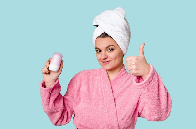 Eine Frau in einem kuscheligen rosa Bademantel und einem Handtuch auf dem Kopf hält ein Deodorant mit einem breiten Lächeln