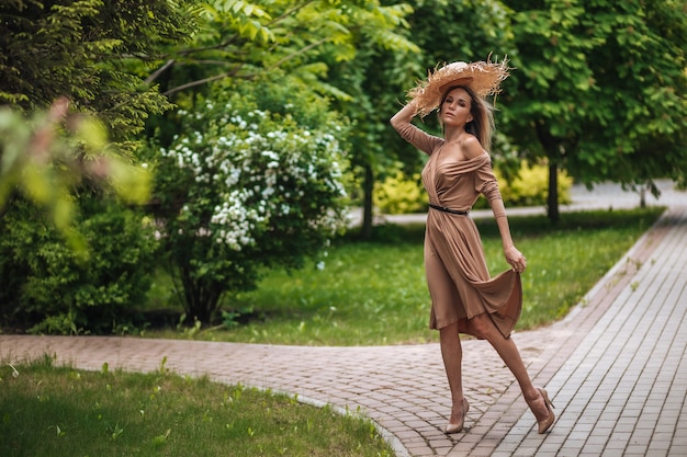 Eine Frau in einem langen braunen Kleid und einem Strohhut spaziert in einem Sommerpark