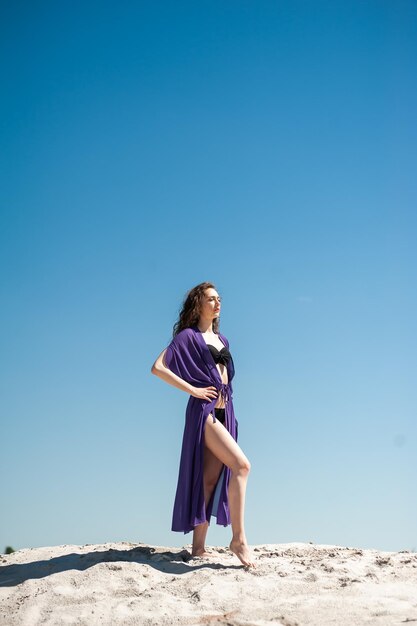 Eine Frau in einem lila Kleid steht auf einem Hügel mit dem Himmel im Hintergrund.