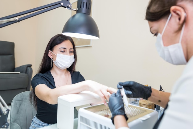 Eine Frau in einem Nagelstudio bekommt eine Maniküre in einem Schönheitssalon von einer Kosmetikerin, die eine Nagelfeile verwendet Nagelpflegekonzept Modellieren von Nägeln Feilen Sie Ihre Nägel mit einer Nagelfeile