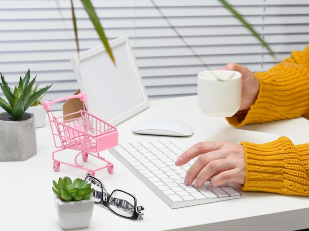 Eine Frau in einem orangefarbenen Pullover sitzt an einem Tisch und arbeitet an einem Computer. Remote-Arbeit, freiberuflich. Online Einkaufen