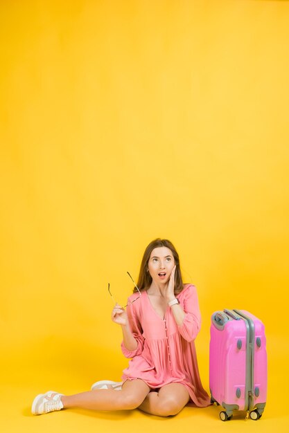 Eine Frau in einem rosafarbenen Kleid hält in ihren Händen eine große rosa Kofferreise