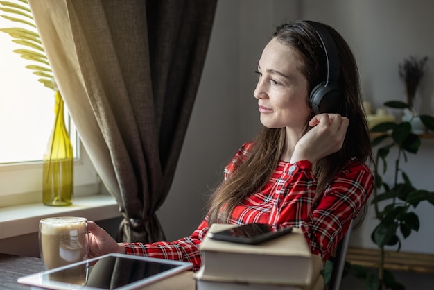 Eine Frau in einem roten Kleid hört Hörbuch mit Kopfhörern Das Konzept der modernen technologischen Bildung und das Studium von Büchern mit Freude