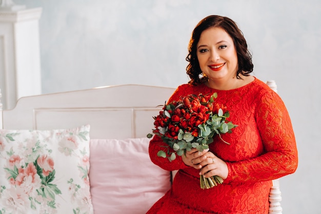 Eine Frau in einem roten Kleid sitzt auf einem Sofa und hält einen Strauß roter Rosen und Beeren im Inneren.