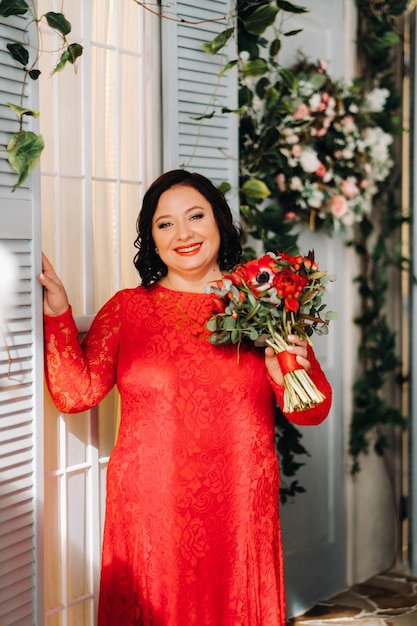 Eine Frau in einem roten Kleid steht und hält einen Strauß roter Rosen und Beeren im Inneren
