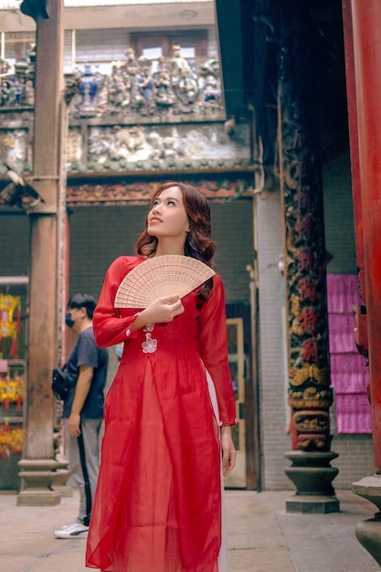 Eine Frau in einem roten Kleid steht vor einem chinesischen Tempel.