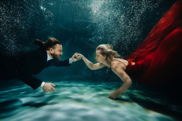 Eine Frau in einem roten Kleid und ein Mann im Anzug treffen sich unter Wasser. Ein Liebespaar unter Wasser