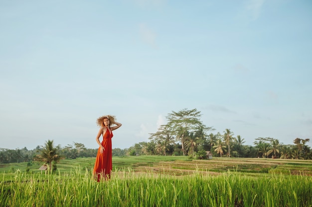 Eine Frau in einem roten Kleid und Hut geht in den Reisfeldern in Bali