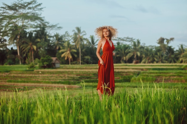 Eine Frau in einem roten Kleid und Hut geht in den Reisfeldern in Bali