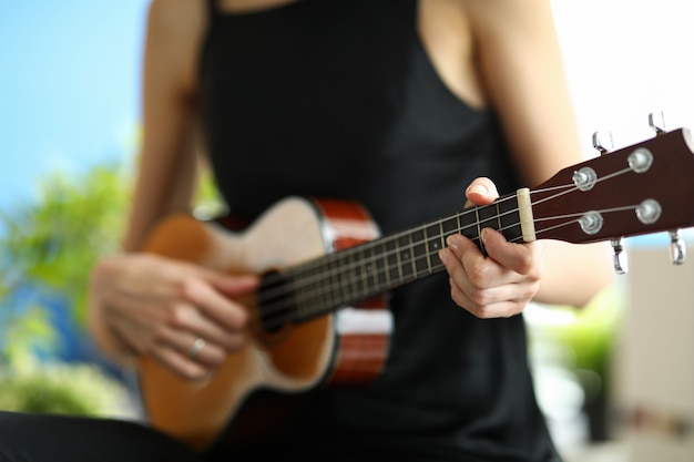 Eine Frau in einem schwarzen Kleid lernt Ukulele zu spielen. Mädchen stimmt eine Miniaturgitarre vor einem Konzert