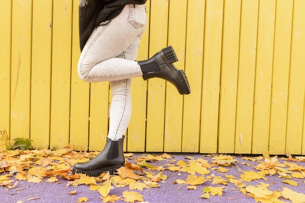 Eine Frau in einem schwarzen Regenstiefel steht vor einer gelben Holzwand.