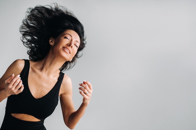 Eine Frau in einem schwarzen Sport-T-Shirt bewegt ihren Kopf mit ihren langen Haaren locker auf einem grauen Hintergrund