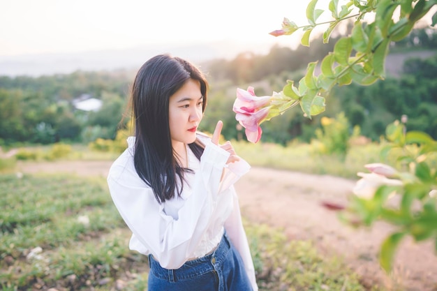 Eine Frau in einem weißen Hemd, die auf eine schöne rosa Blume in einem Garten mit Blick auf die Natur zeigt