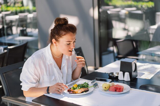 Eine Frau in einem weißen Hemd isst Mittag- oder Frühstück im Freien in einem Café
