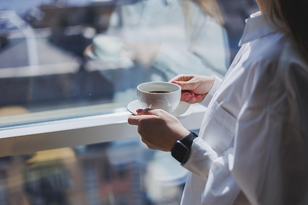 Eine Frau in einem weißen Hemd mit duftendem heißem Kaffee in ihren Händen Closeup Frauenhände mit einer Tasse Americano selektiven Fokus