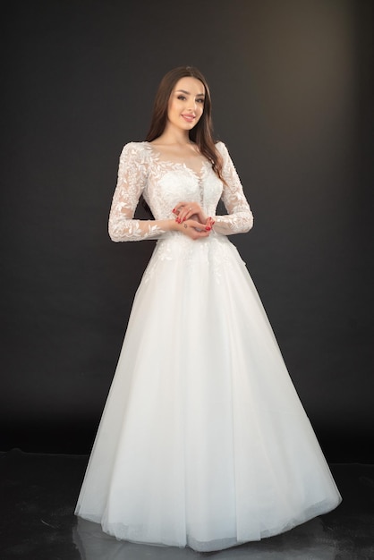 Eine Frau in einem weißen Hochzeitskleid steht vor einem schwarzen Hintergrund.