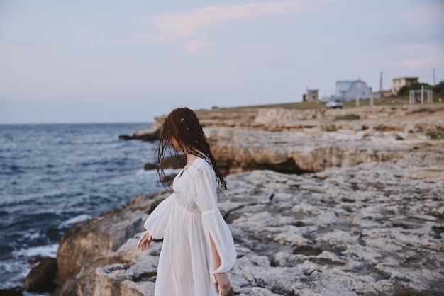 Eine Frau in einem weißen Kleid geht auf den Felsen am Meer spazieren