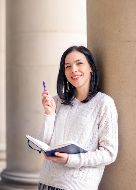 Eine Frau in einem weißen Pullover mit einem Notizbuch, das draußen Ideen aufschreibt
