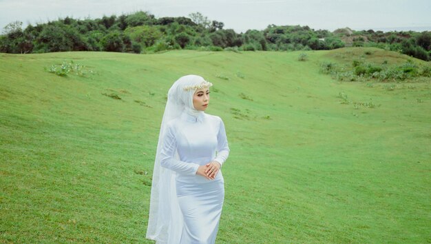 Eine Frau in einem weißen Schleier geht über ein Feld.