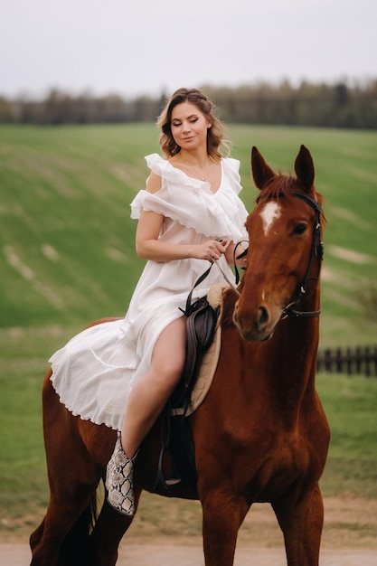 Eine Frau in einem weißen Sommerkleid, die auf einem Pferd auf einem Feld reitet