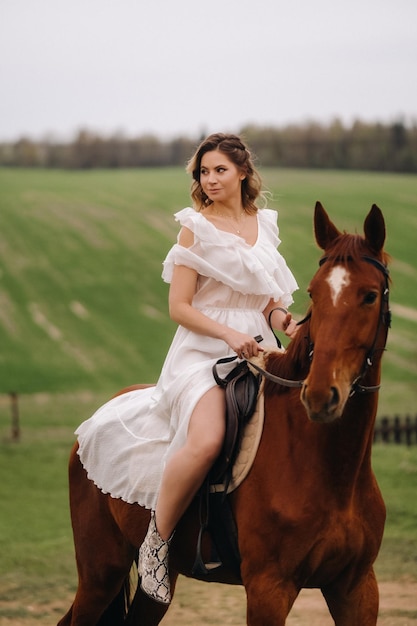 Eine Frau in einem weißen Sommerkleid, die auf einem Pferd auf einem Feld reitet