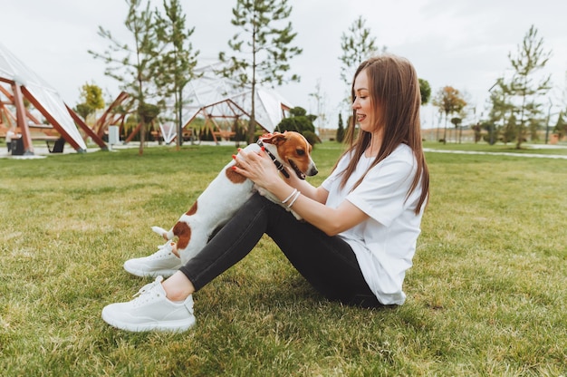 Eine Frau in einem weißen T-Shirt und Jeans umarmt ihren Jack Russell Terrier Hund in der Natur im Park Loyale beste Freunde seit Kindheit Lifestyle