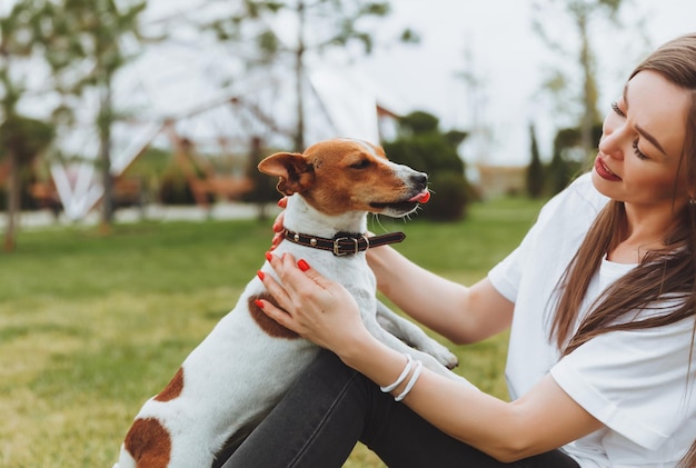 Eine Frau in einem weißen T-Shirt und Jeans umarmt ihren Jack Russell Terrier Hund in der Natur im Park Loyale beste Freunde seit Kindheit Lifestyle