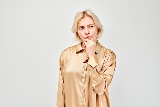 Eine Frau in einer beigefarbenen Bluse, die mit einem nachdenklichen Ausdruck überlegt, isoliert auf einem hellen Hintergrund