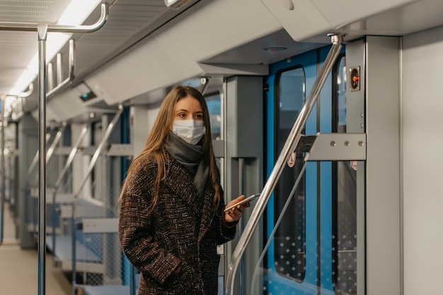 Eine Frau in einer medizinischen Gesichtsmaske zur Vermeidung der Ausbreitung des Coronavirus steht in der Nähe von Türen und starrt in einem leeren U-Bahn-Wagen zur Seite. Ein Mädchen in einer chirurgischen Maske fährt mit einer U-Bahn.